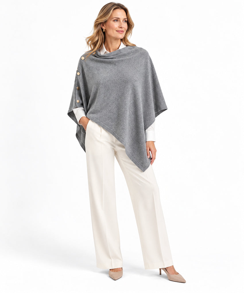 Woman wearing grey pure cashmere poncho shawl with side buttons, styled with white trousers by Moda de la Maria