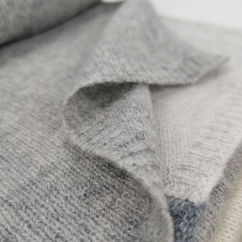 Detailed view of a Moda de la Maria luxury 100% pure cashmere scarf in grey and cream, showcasing the fine knit, colour-block design and premium natural fibres.