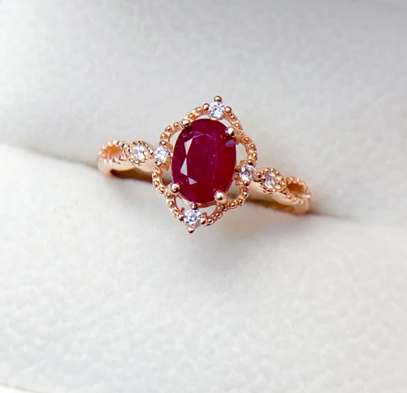 Close-up of natural oval ruby gemstone with halo of white cubic zirconia in rose gold setting.