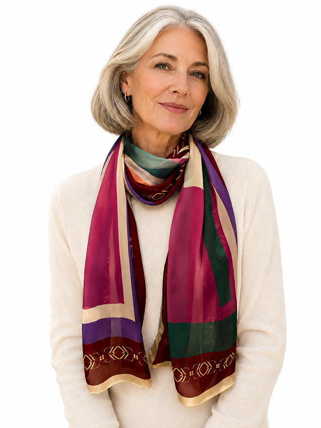 Elegant mature woman wearing a colourful long silk chiffon scarf with burgundy and geometric detailing, styled with luxury knitwear on a white background by Moda de la Maria.