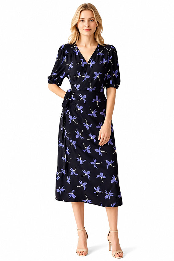 Blonde model wearing a luxury navy floral wrap dress with lavender botanical print by Moda de la Maria on a white background.