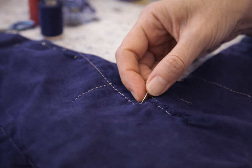 Close-up of hand stitching repairing a hole in denim during a private mending and repair sewing class in London.