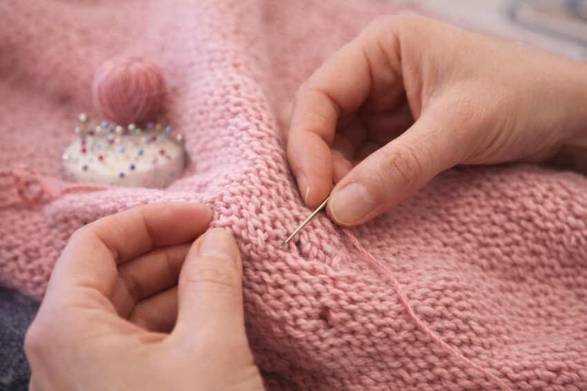Repairing a hole in a knitted sweater using hand stitching techniques during a private clothing repair class in London.