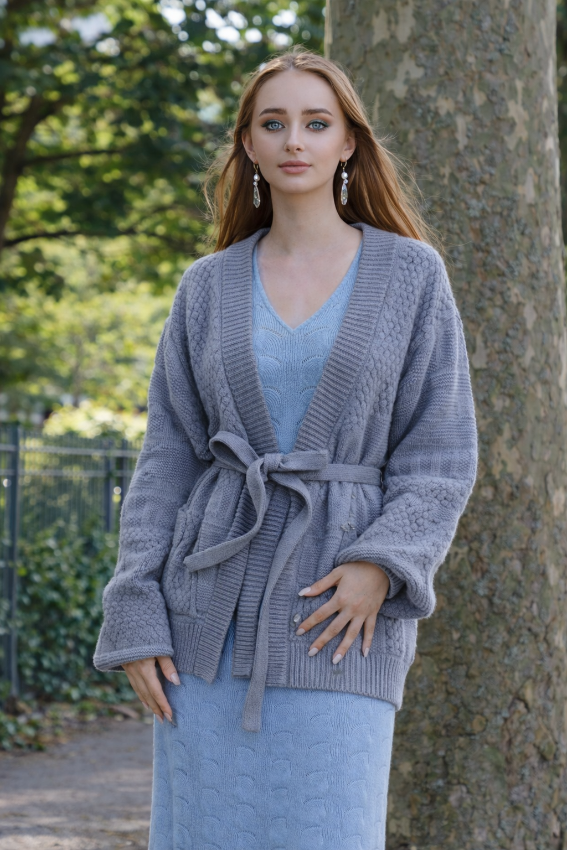 Grey cable knit belted cashmere cardigan for women by Moda de la Maria worn over a light blue knit dress in a natural outdoor setting