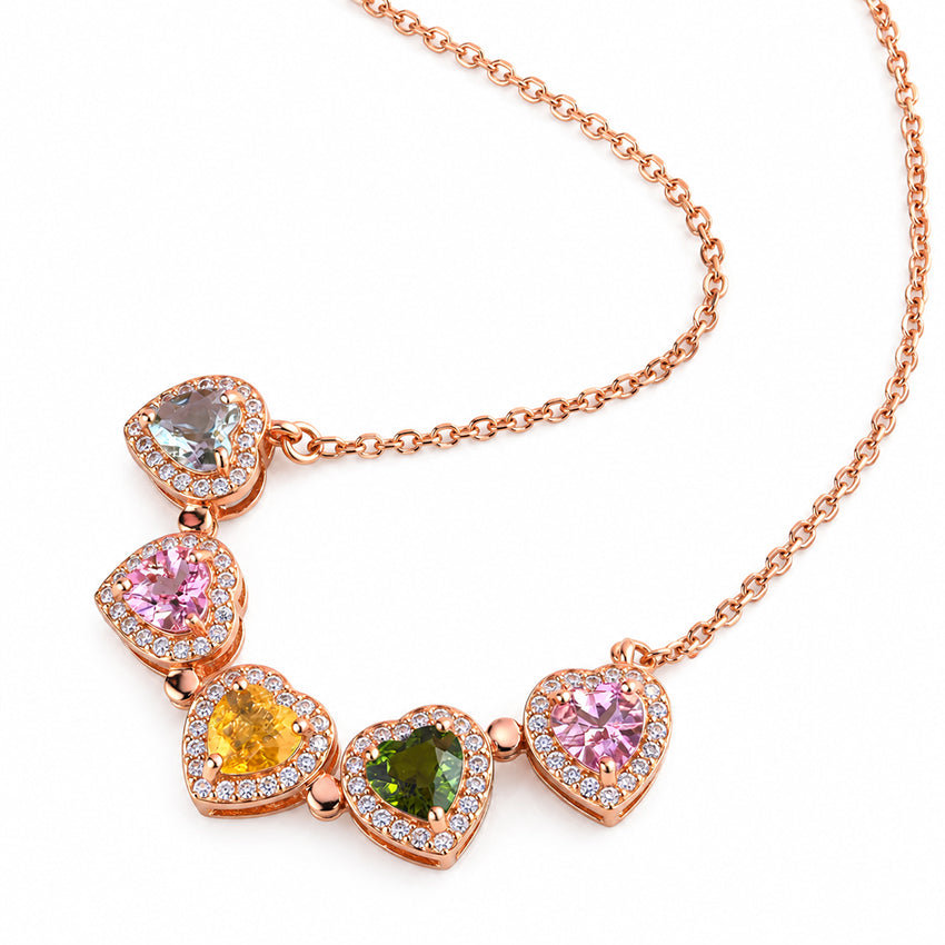 Close-up of five multicolour heart-shaped gemstones in rose gold settings on a Moda de la Maria necklace.