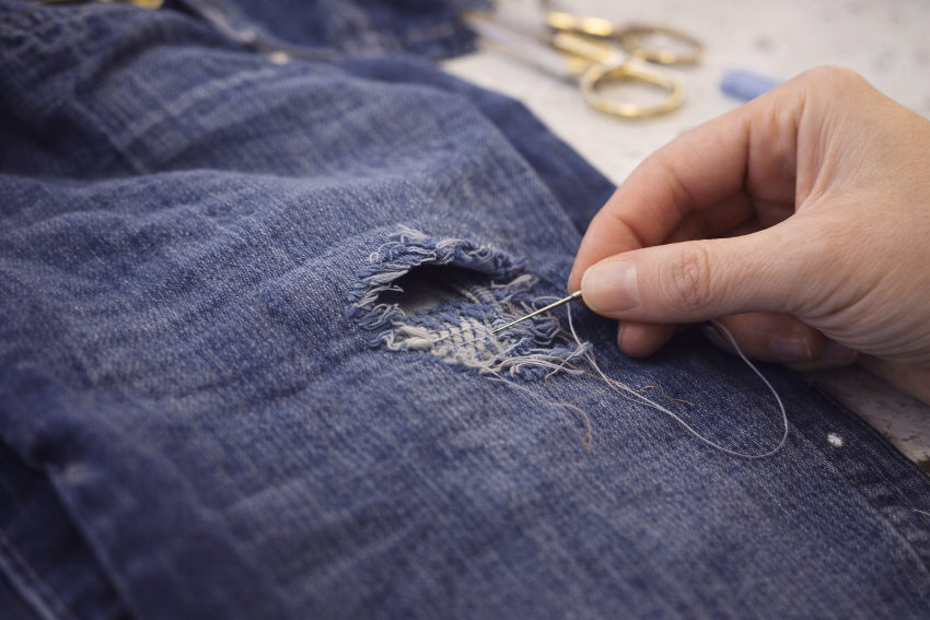 Repairing damaged denim with a fabric patch during an advanced garment repair sewing workshop in London.