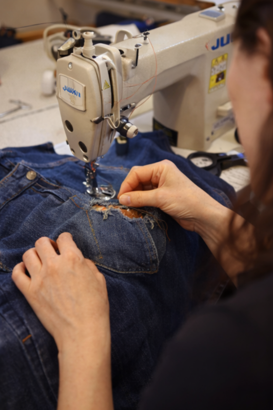 Using a sewing machine to reinforce a repaired garment during an advanced clothing repair workshop in London.