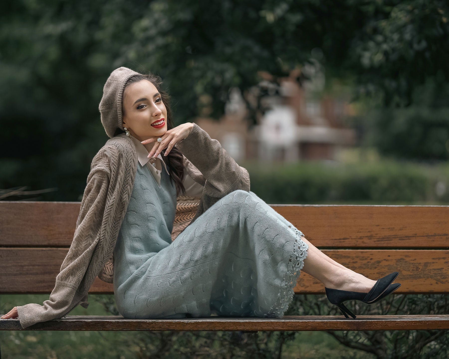 Model seated on a park bench wearing a blue cashmere dress over a silk shirt, styled with a scarf and hat for an elegant layered look by Moda de la Maria.